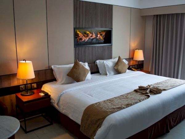 A neatly arranged hotel room with a large bed, soft lighting, two bedside lamps, and a decorative towel swan on the bed.
