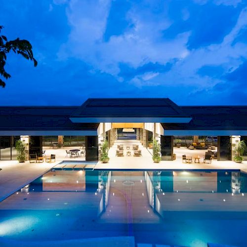 An illuminated outdoor pool area of a modern building at dusk, reflecting the vibrant sky and spacious layout.