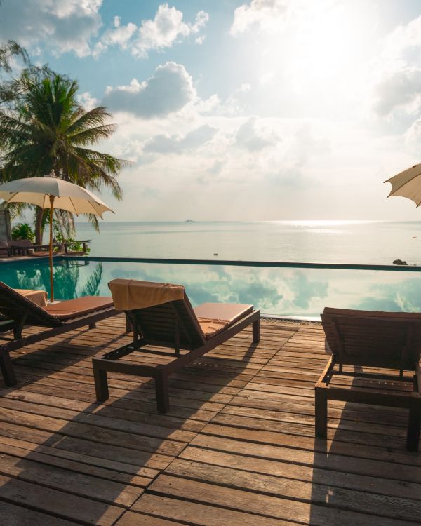 A serene beachside scene with lounge chairs and umbrellas on a wooden deck, overlooking a tranquil sea under a partly cloudy sky.