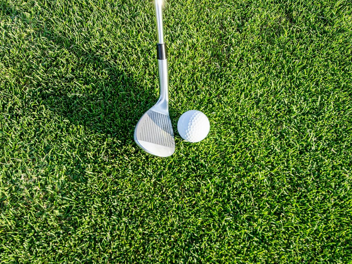 A golf club and ball are shown on a well-manicured patch of green grass, ready for a golf game.