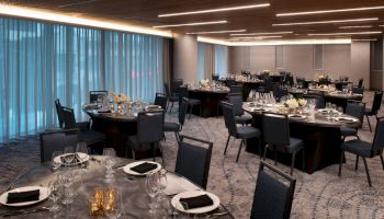 This image shows an elegantly set banquet hall with round tables and chairs, each table adorned with black napkins, glassware, and floral centerpieces.