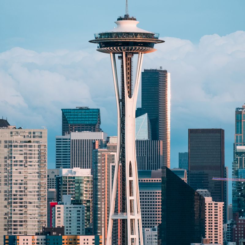 The image shows the Space Needle, a prominent observation tower, with Seattle's city skyline in the background and cloudy skies above.