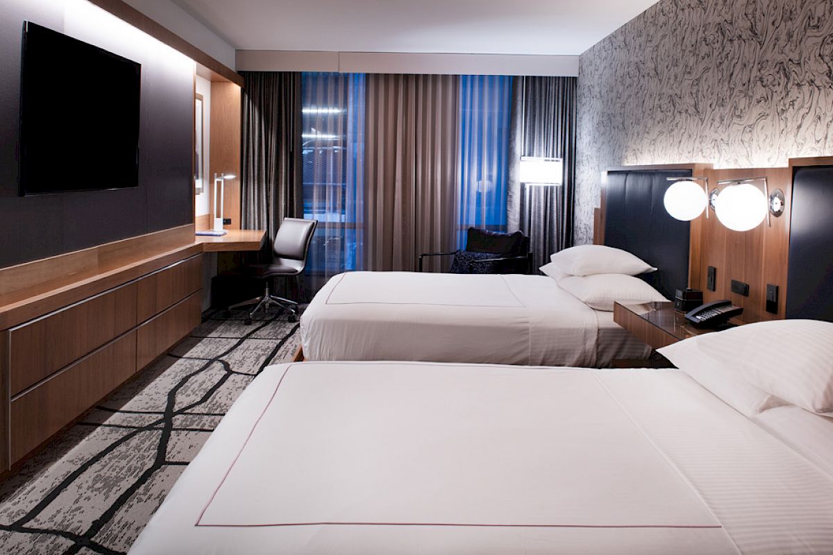 A modern hotel room with two neatly made beds, a wall-mounted TV, a desk with a chair, and stylish decor.