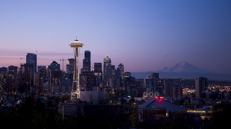 This image shows the Seattle skyline at dusk, featuring the Space Needle and surrounding buildings with Mount Rainier visible in the background.